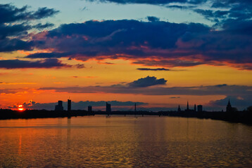 Fototapeta premium sunset. in the photo, the clouds are illuminated by the evening sun,in the foreground is a river, in the background is a city