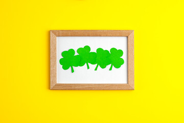 Four green paper clovers flat lay top view on wooden frame in the centre on yellow background Saint Patrick's Day 17 march traditional spring celebration holiday and good luck concept
