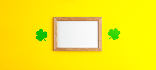 Green paper clovers flat lay mockup banner on wooden frame in the centre with white copy space on yellow background Saint Patrick's Day 17 march traditional spring celebration holiday good luck