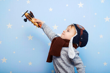 Little boy in helmet and glasses with wooden plane against the background of a blue wall with...