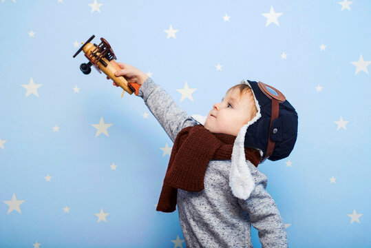 Little boy in helmet and glasses with wooden plane against the background of a blue wall with stars. Happy child playing with toy airplane
