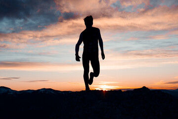 PERSON RUNNING AT THE TOP OF A MOUNTAIN. MAN ENJOYING AND HAVING FUN DURING SUNSET. OUTDOOR AND SUNSET CONCEPT.