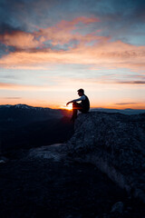 Obraz premium PERSON SITTING AT THE TOP OF A MOUNTAIN. MAN ENJOYING AND HAVING FUN DURING SUNSET. OUTDOOR AND SUNSET CONCEPT.