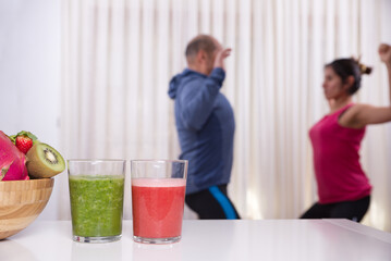 Smoothies and fruits in focus and people exercising in the background out of focus