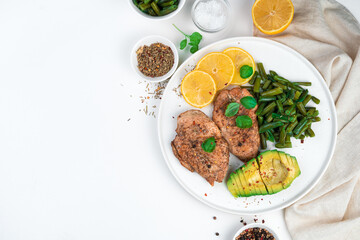 Chicken breast, avocado and string beans with basil on a flat plate on a light background. Healthy food. Top view, horizontal, with space to copy.