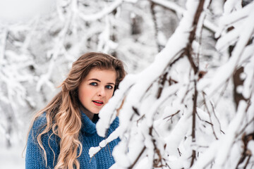 beautiful winter girl in a blue cozy knitted sweater playing with snow