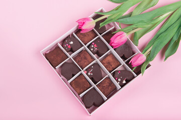 Present box with chocolate sweets hearts and tulips on pink background. Desert for Valentine Day