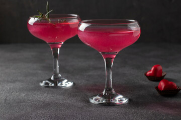 Two glasses of shimmering pink champagne and heart-shaped candies on a dark background. Romantic dinner for a couple.