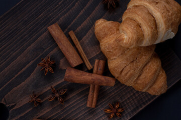 Fresh croissant with chocolate and cinnamon sticks on wooden background 