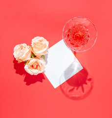 Roses and glass of juice on red background with blank paper card. Flat lay concept. Copy space.