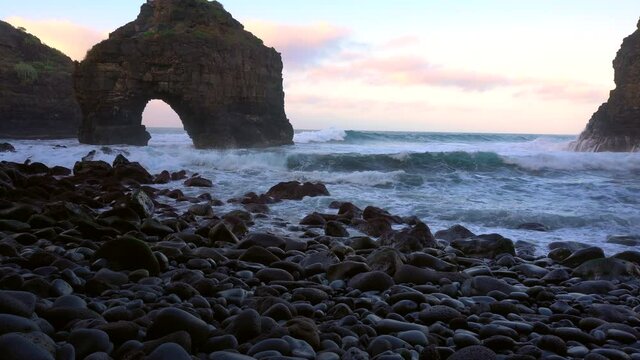 Waves crash on volcanic cliff and flow through an arc. High breakers wash up on the stony beach in los roques tenerife spain