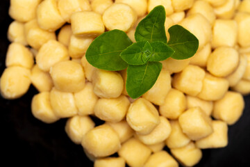 Pile of fresh raw gnocchi with basil leaves, view from above on a black dish