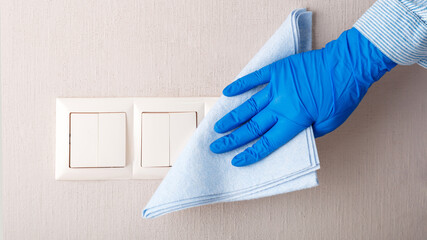 Light switch surfaces disinfection. Woman in rubber blue glove clean light switch with cloth on...