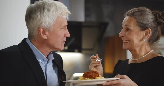 Senior woman feeding husband with delicious pasta having dinner at home