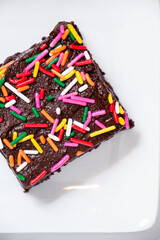 homemade chocolate frosted brownies with rainbow colored sprinkles on a white background