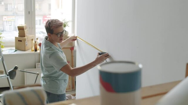 Young woman using tape measure while measuring wall in room under renovation