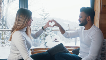 Young couple making heart shape with hands near the window on Valentines day date. High quality photo