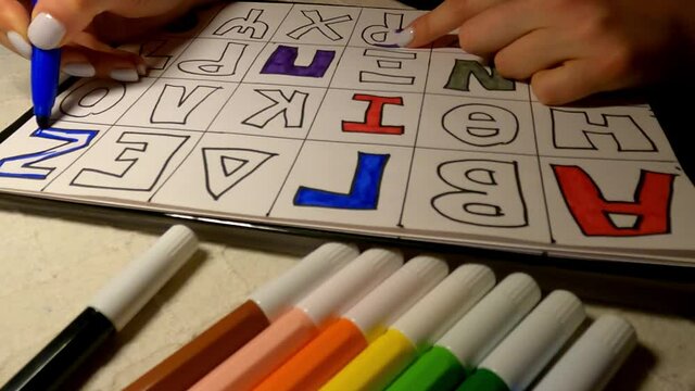 Preschool female teacher coloring letters of greek alphabet letters with colored marker.Concept of education from home during quarantine.Distance education. E-learning for children.