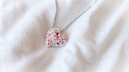 A beautiful pale pink heart pendant with a silver chain, isolated and contrasted against a white bed spread in London, Ontario, Canada.