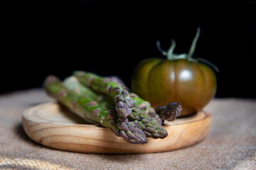 Fresh and organic green tomatoes and some asparagus, on a wooden table.