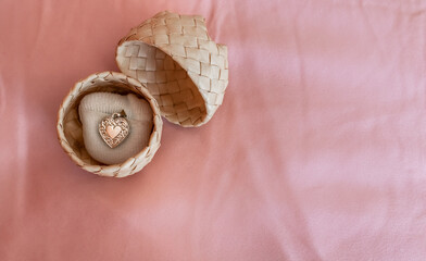 A silver heart-shaped locket on a small white pillow in a woven palm ring box on a pink silk...