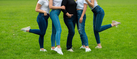 four girls in white t-shirts and blue jeans on a green lawn posing for a photo