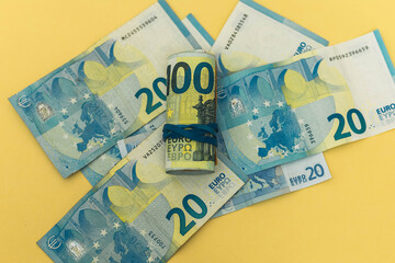 background of twenty euro banknotes on yellow color and a roll of banknotes held by a rubber band
