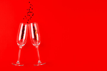Two champagne glasses with red heart shaped confetti over red background. Festive mood. Overhead view, copy space. Celebration party concept