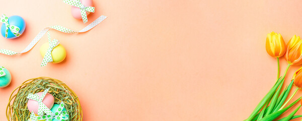 Easter bunny. Colourful egg with tape ribbon, spring tulips, feathers on pastel pink background in Happy Easter decoration. Traditional banner in top view.