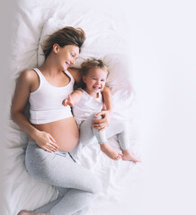 Pregnant mother and daughter resting in bed. Young woman with her first child during second...
