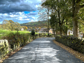 Obraz premium Country lane, leading from, Butterworth Lane, with fields, housing, and distant hills in, Triangle, Ripponden, UK