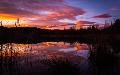 Obraz premium Spectacular sunset with orange and red clouds reflected in the lake water. Natural mirror at sunrise. Estany de Banyoles, Girona, Catalonia, Spain.
