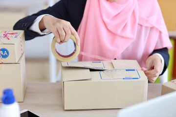 Closeup active asian muslim woman hands in blue suit sitting and working on online package box delivery. Startup small business SME freelance girl working on computer and mobile phone with happy face