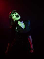 Fototapeta na wymiar girl in green-red with vampire fangs on a dark background