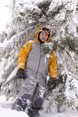 Male snowboarder in gray and orange jumpsuit standing in a winter forest. Winter active rest. Vacation in the mountains. Healthy lifestyle.