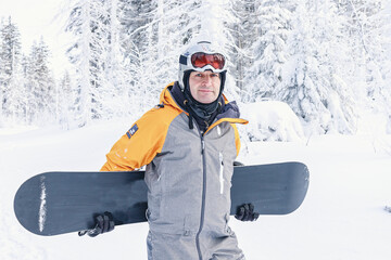 Man with a snowboard standing on a mountain on the background of the winter forest. Winter leisure activity. Healthy lifestyle. Extreme sports.