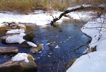 Boulders covered with snow for a path crossing a stream in the woods after a winter storm in New Jersey
