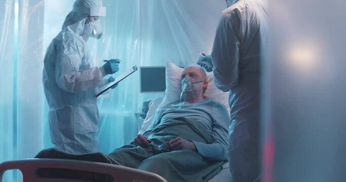 Doctors in protective overall scanning temperature of patient and writing down results