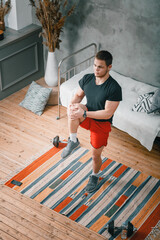 A cheerful athlete with black  hair  lunges,  stretching  in the bedroom, next to a laptop with online training. The young man goes in for sports at home.