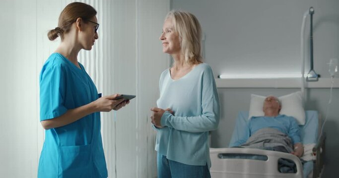 Smiling aged woman talking to doctor discussing sick husband recovery