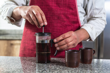 Fototapeta na wymiar Close-up of a man's hands in a red apron pressing coffee in a French press