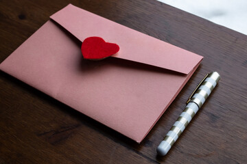 A salmon coloured envelope holding a wedding invitation with a red felt heart as the seal, next to...