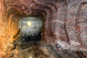A miner examines a mine, illuminating the walls with his flashlight