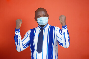 An African man with nose mask raising his hands with his fist clenched up in jubilation 