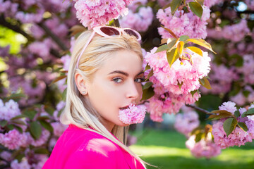 Fototapeta premium Beautiful girl in pink flowers in summer blossom park. Portrait of young woman in the flowered garden in the spring. Tongue sensual.