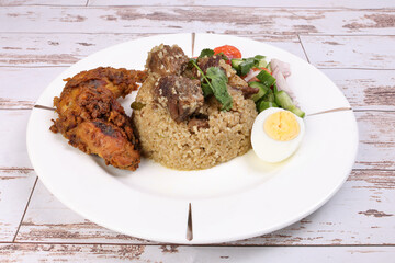 Beef Biryani Tehari with boiled egg coriander leaf garnish chicken curry pot roasted leg tomato cucumber onion chili coriander salad on white plate set over rustic wood background