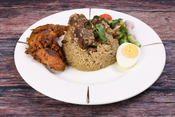 Beef Biryani Tehari with boiled egg coriander leaf garnish chicken curry pot roasted leg tomato cucumber onion chili coriander salad on white plate set over rustic wood background