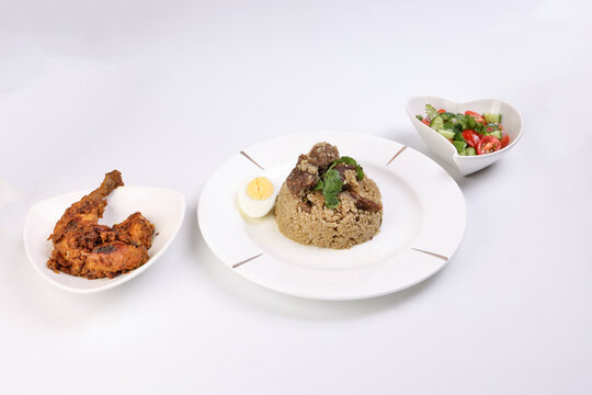 Beef Biryani i with boiled egg coriander leaf garnish on white plate chicken curry pot roasted leg triangle dish tomato cucumber onion  coriander salad hart shape dish set over white background