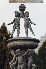 Fountain bowl with cupids in the form of small children with cypresses in the background. A...