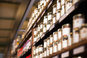 Rows of glass jars with natural spices and herbs lined up on shelves in grocery store